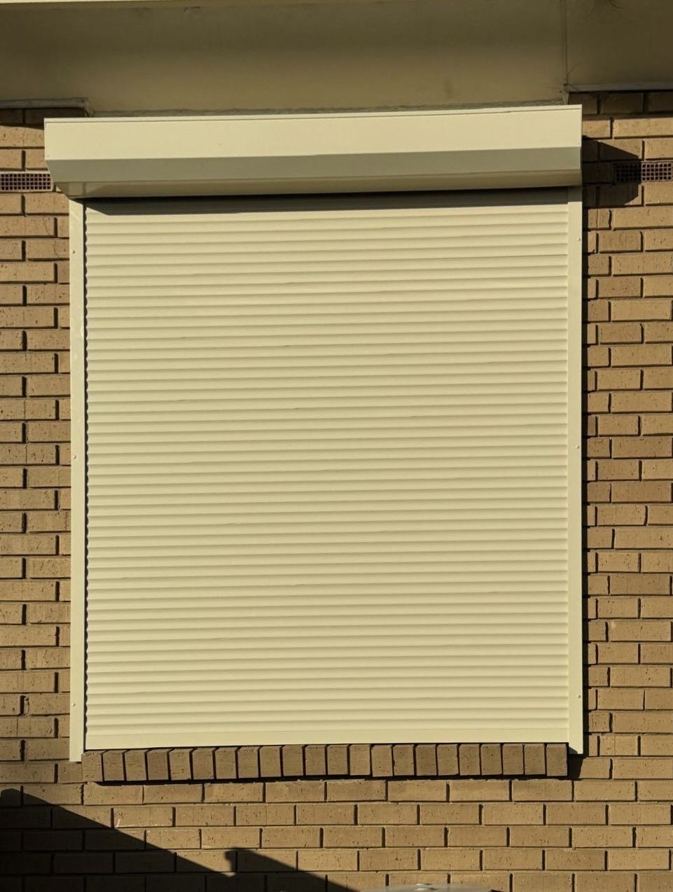 Cream roller shutter on brick home